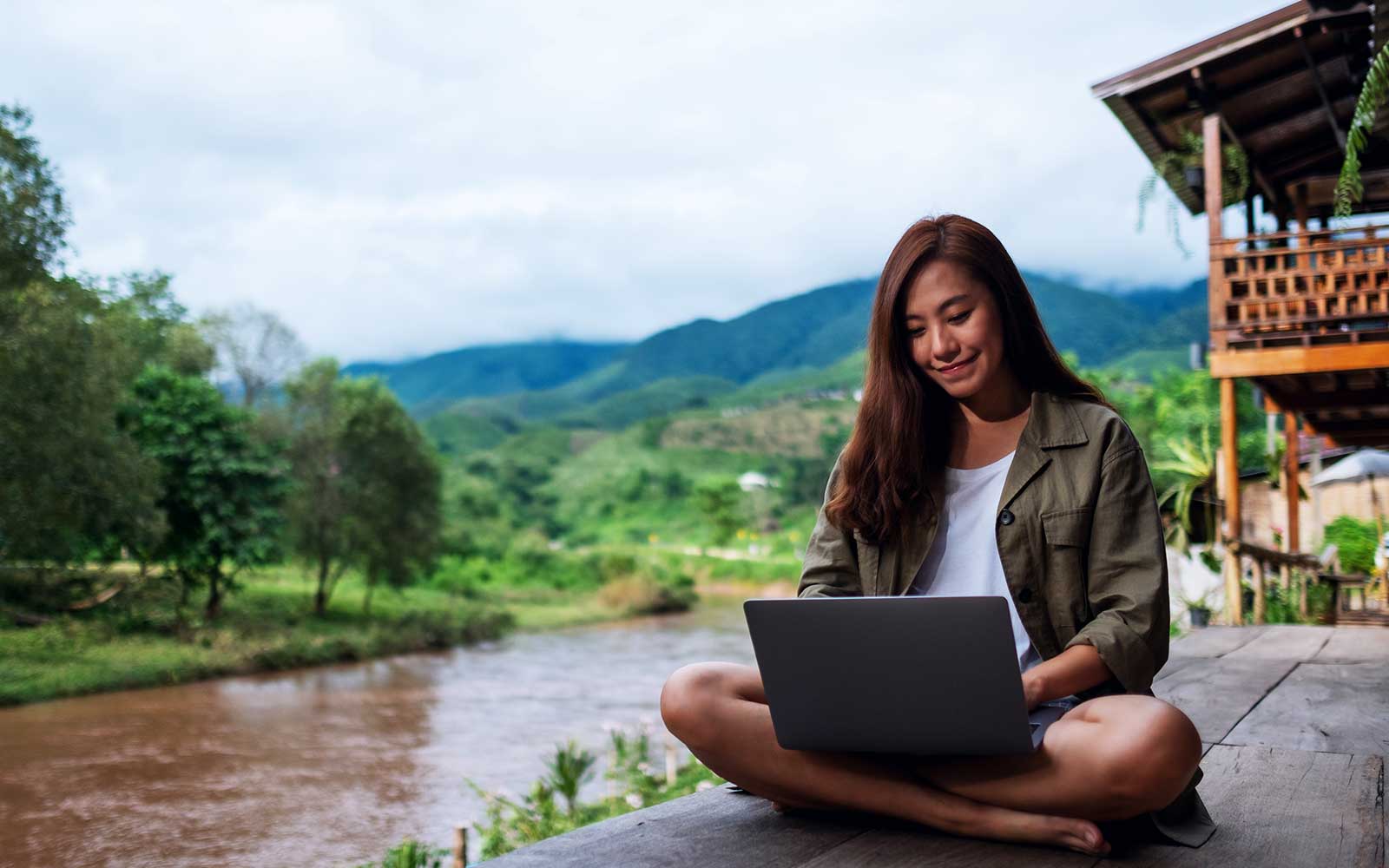 A remote worker using a laptop beside a mountain river